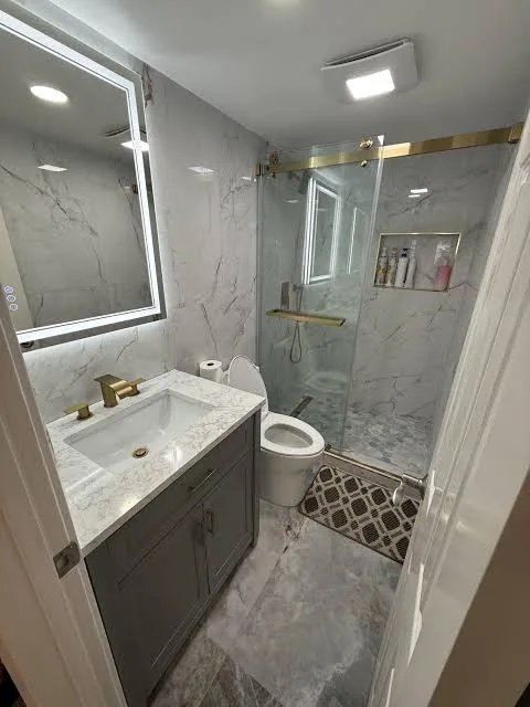 Compact remodeled bathroom with marble-look tile, gray vanity and gold shower hardware